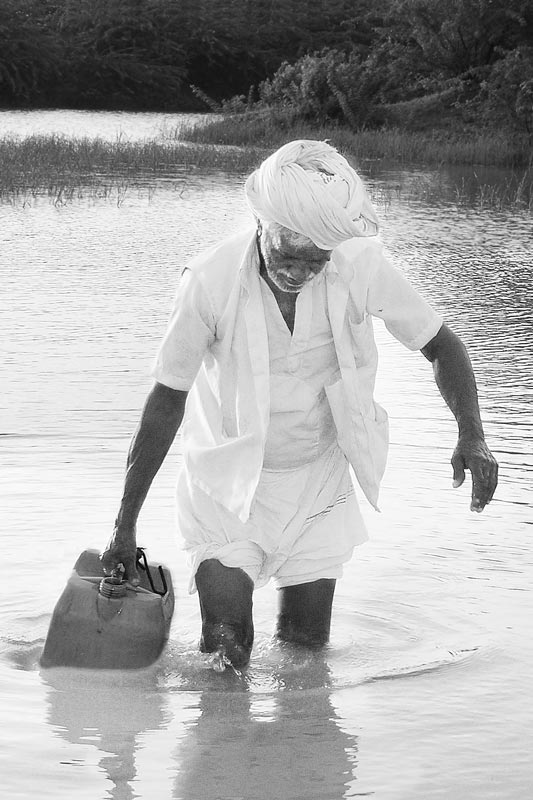 Water portraits - An old villager who supports his family in water procurement as a routine by filling cans from a distant pond, transporting these home on his bicycle – Bhavnagar district, Gujarat